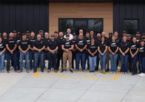 A roofing team poses for a group photo outside their company building.