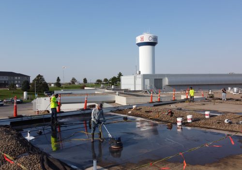 Roofers conduct maintenance on a commercial rooftop under a clear blue sky.
