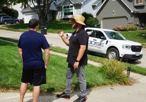Roofer discusses roofing project with homeowner in a suburban neighborhood.
