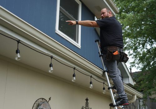 Roofer inspecting upper window from a ladder outside a home.