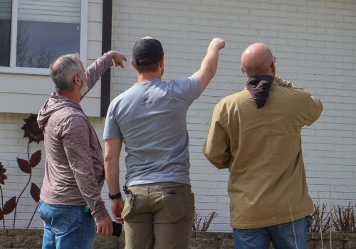 Three men inspecting a home roof for potential repair or maintenance needs.