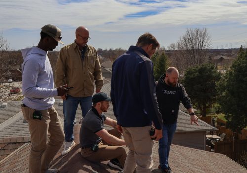 Roofing professionals inspect and discuss repairs on a residential rooftop.