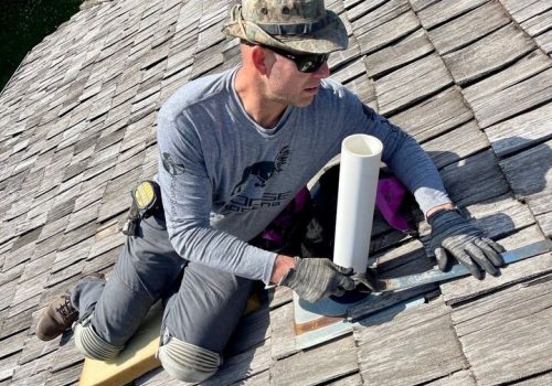 Roofer working on a shingle roof with tools and protective gear.