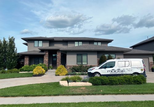 A modern two-story house with a roofing service van parked in the driveway.