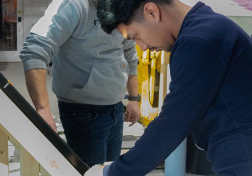 Roofing professionals examining shingles in a workshop environment.